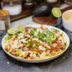 A white bowl of street corn taco salad. The base is Romaine lettuce with tomatoes, corn, tortilla strips, avocado and a creamy dressing.