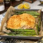 A filet of baked panko crusted salmon with asparagus on a parchment-lined baking sheet. The salmon has a browned crust.