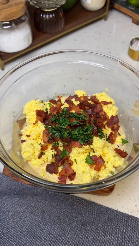 Hardboiled eggs that have been fluffed in a food processor in a glass bowl with crisp, diced bacon, fresh parsley and a mayo-based sauce