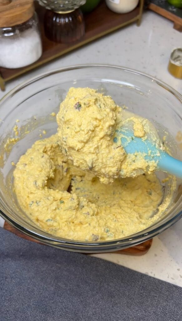 Egg Salad with Bacon mixed together in glass bowl. The photo is showing some of the mixture on a rubber spatula.