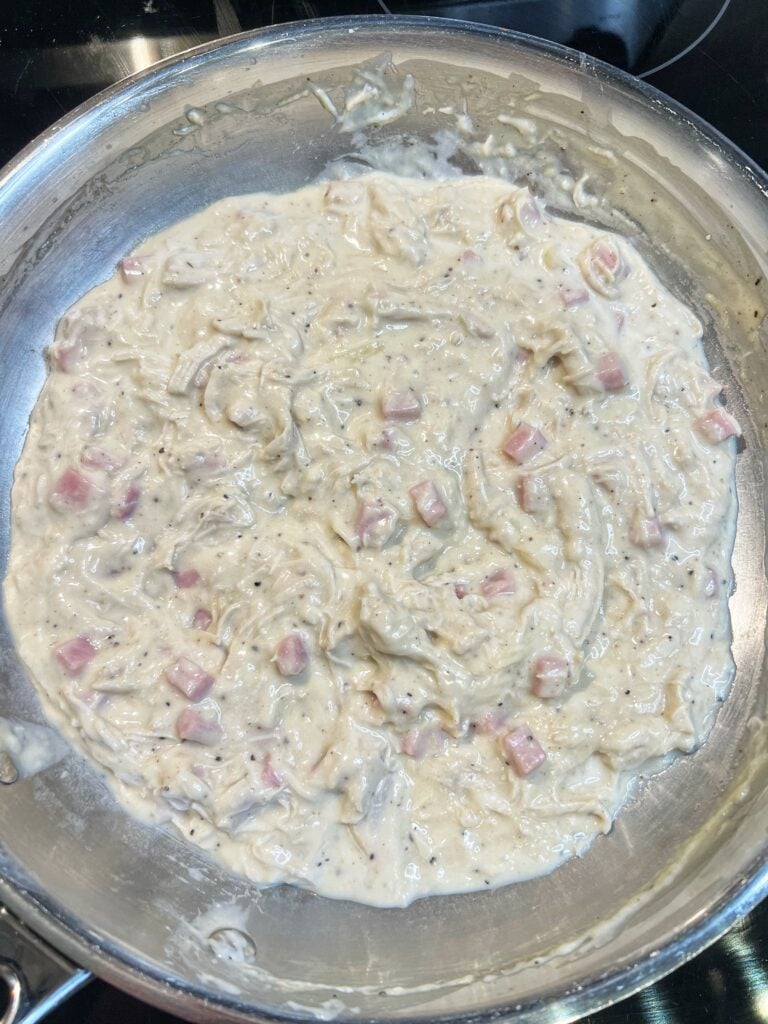 Chicken Cordon Bleu pot pie mixture in a pan. The sauce is creamy with shredded chicken and diced ham.