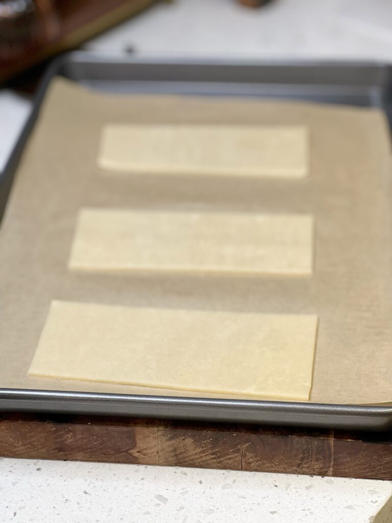 A frozen pie crust cut into three rectangular pieces. All are sitting on a parchment-lined baking sheet.