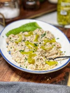 A platter of pepperoncini tuna salad. The tuna salad is mayo-based and is garnished with fresh parsley, sliced pepperoncini peppers, and sliced avocado.