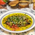 Ingredients in a plate for Rustic Bread Dipping Oil. There is olive oil, balsamic vinegar, crushed olives, fresh herbs and diced tomatoes.