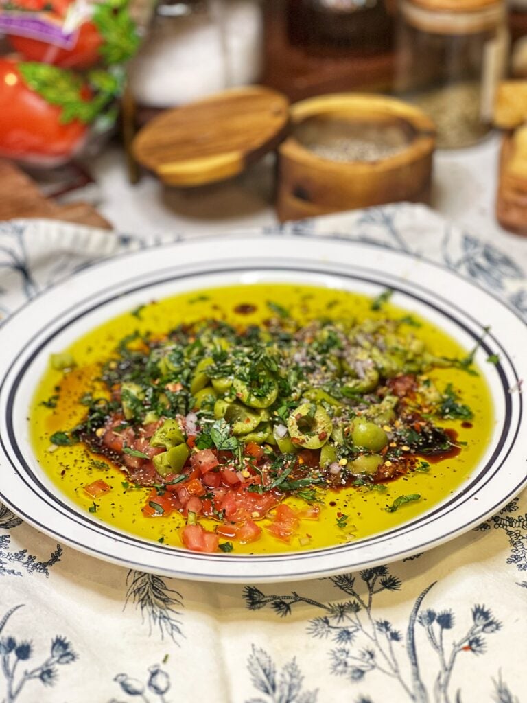 Ingredients in a plate for Rustic Bread Dipping Oil. There is olive oil, balsamic vinegar, crushed olives, fresh herbs and diced tomatoes.