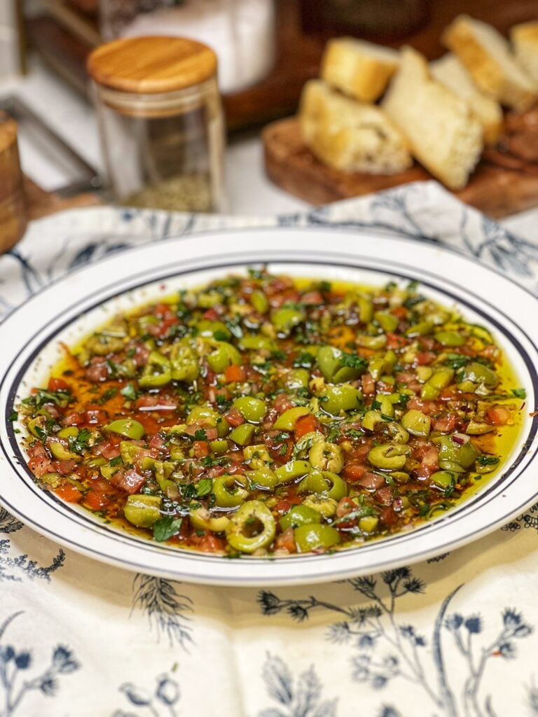Rustic Bread Dipping Oil on a plate. It's a mixture of olive oil, balsamic vinegar, chopped olives and tomatoes, and fresh herbs.