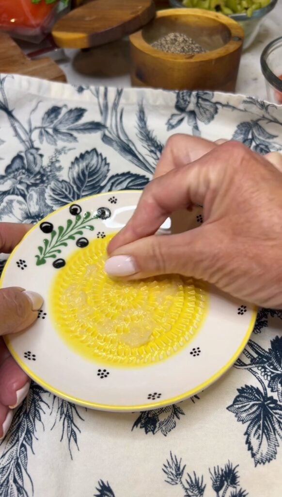 Grating a garlic clove on a small plate that has grooves for grating.