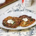 Two potato and cheese pancakes on a white platter. Each are topped with a dollop of sour cream and garnished with fresh parsley.