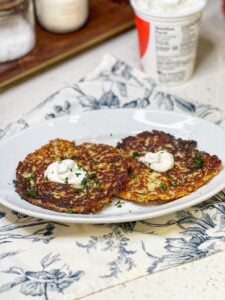 Two potato and cheese pancakes on a white platter. Each are topped with a dollop of sour cream and garnished with fresh parsley.