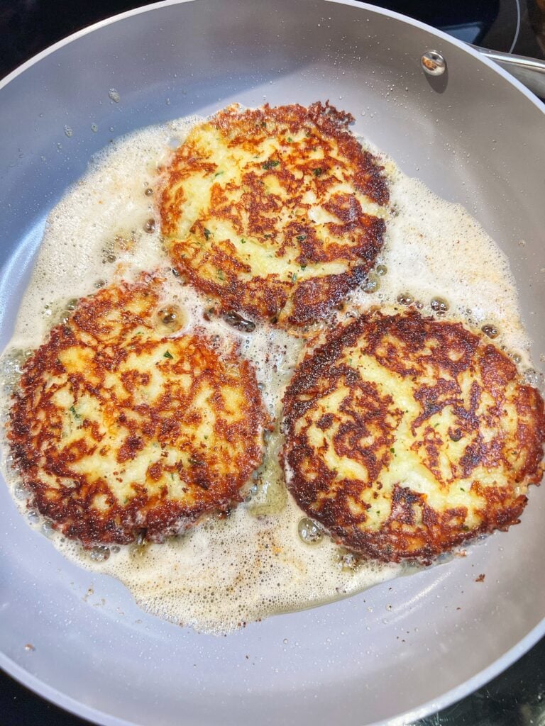 Frying three potato and cheese pancakes in a non-stick pan. The pancakes are browned on the top.