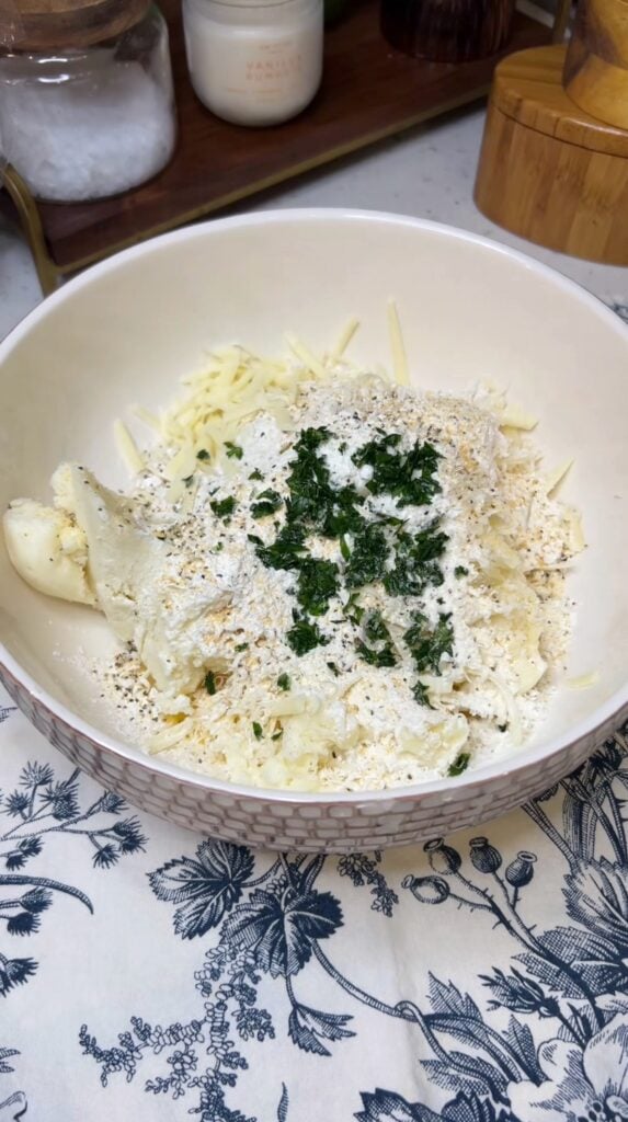 Mashed potatoes, cheese, flour, spices and fresh parsley in a bowl.