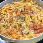 A pan of peppercorn chicken pasta with mushrooms. Pappardelle pasta is in a creamy mushroom sauce with seared chicken breasts.