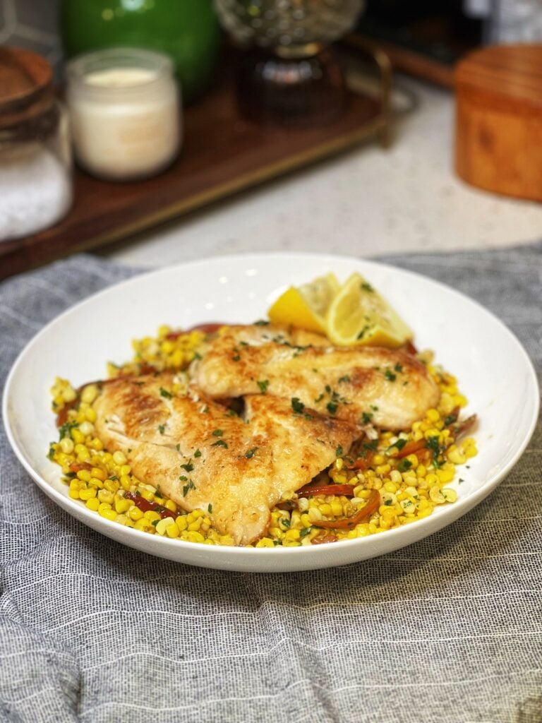 Two pan sautéed trigger fish resting on a bed of brown butter corn in a bowl.