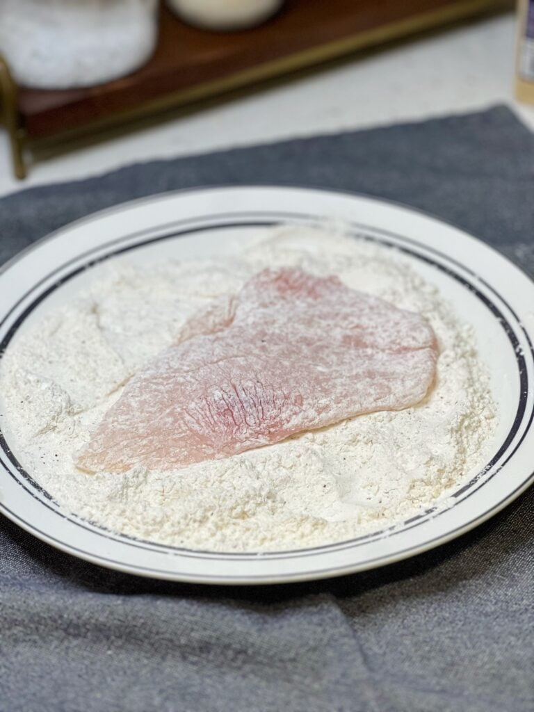A filet of trigger fish dredged in flour sitting in a plate of the flour dredge.