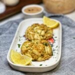 Two baked jumbo lump crab cakes on a platter with lemon wedges.