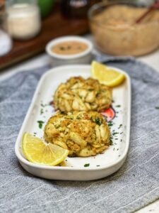 Two baked jumbo lump crab cakes on a platter with lemon wedges.