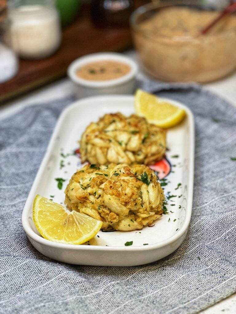 Two baked jumbo lump crab cakes on a platter with lemon wedges.