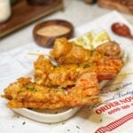 Three deep fried lobster tails in a white tray with lemon wedges and garnished with fresh parsley.
