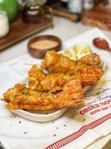 Three deep fried lobster tails in a white tray with lemon wedges and garnished with fresh parsley.
