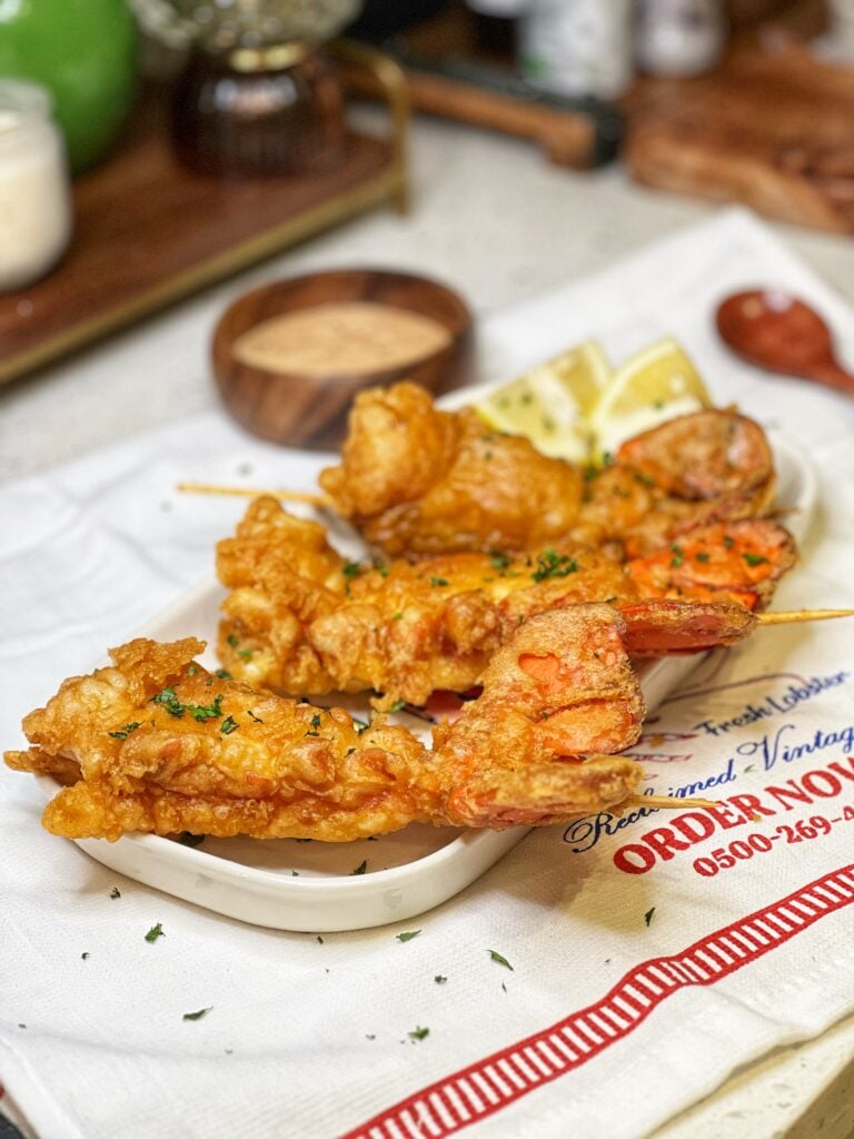 Three deep fried lobster tails in a white tray with lemon wedges and garnished with fresh parsley.