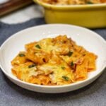 A white, shallow bowl filled with a few spoonfuls of baked rigatoni in a meat and béchamel sauce that has browned cheese on top. The dish is garnished with fresh basil.