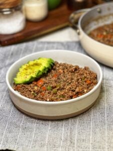 A white bowl filled with steamed rice and topped with Black Pepper Ground Beef, and sliced avocado.