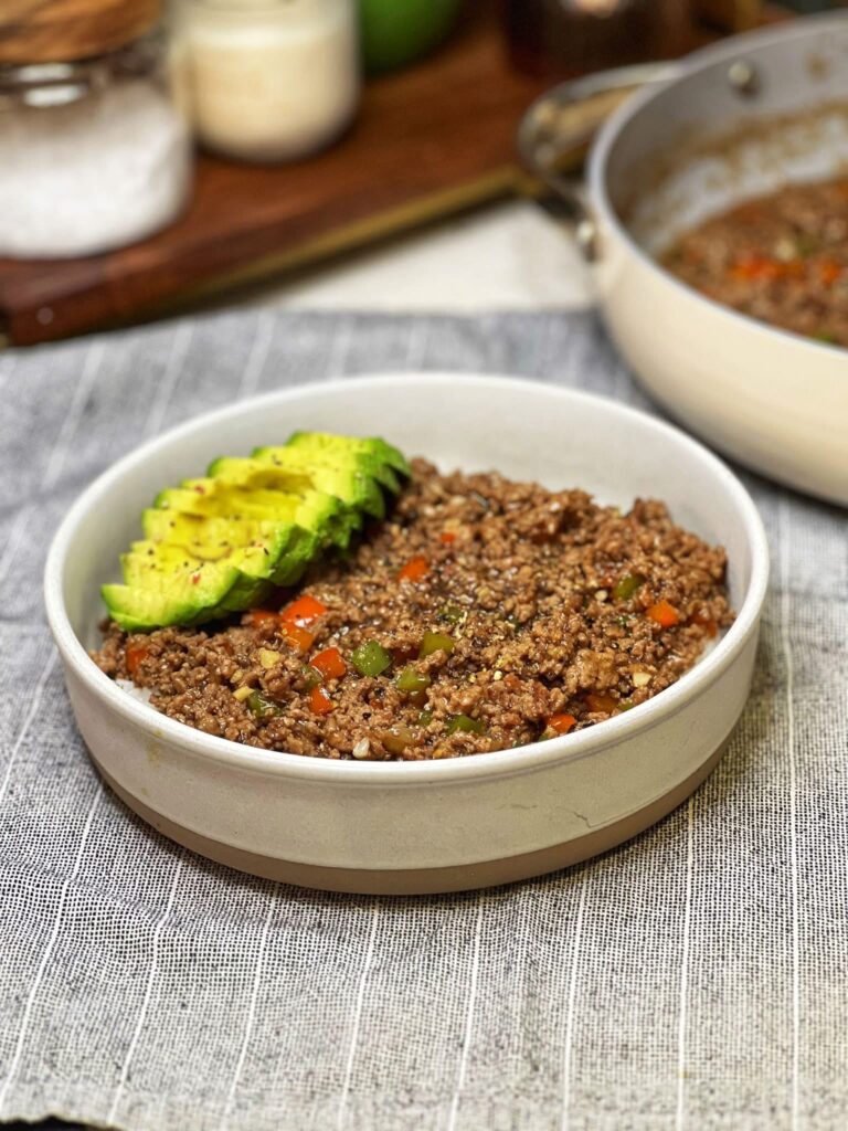 A white bowl filled with steamed rice and topped with Black Pepper Ground Beef, and sliced avocado.