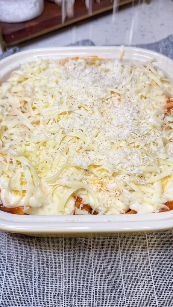 An unbaked casserole dish of baked rigatoni with meat sauce topped with shredded mozzarella and Parmesan cheese.