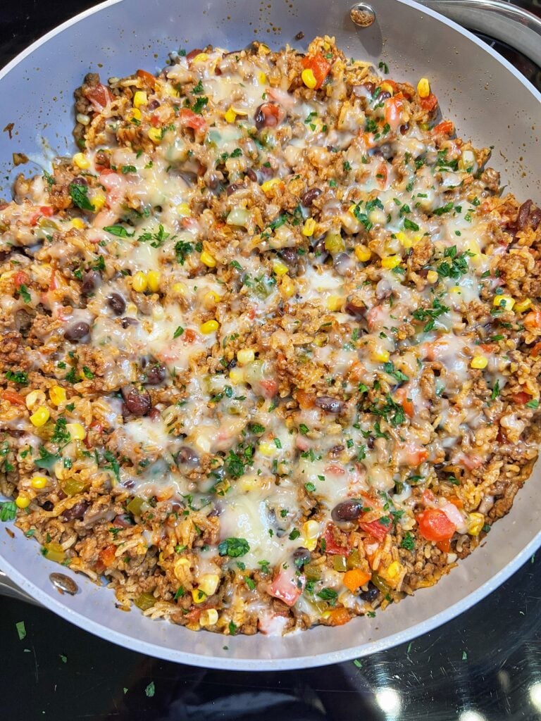 A beef taco rice skillet. Browned ground beef was cooked with rice, peppers, corn and black beans then topped with shredded cheese that is melted on the top.
