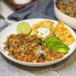 A shallow bowl with a few spoonfuls of beef taco rice, sliced avocado, a lime wedge, and triangles of cheese quesadillas topped with sour cream.