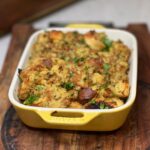 A casserole dish of baked, homemade herb stuffing. The top is browned and garnished with fresh parsley.