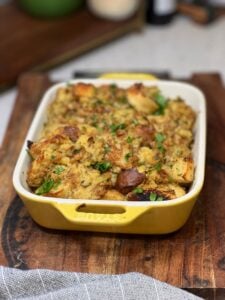 A casserole dish of baked, homemade herb stuffing. The top is browned and garnished with fresh parsley.