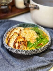 A curry chicken rice bowl. Steamed rice is in a bowl with snow peas, chicken and a creamy broth.