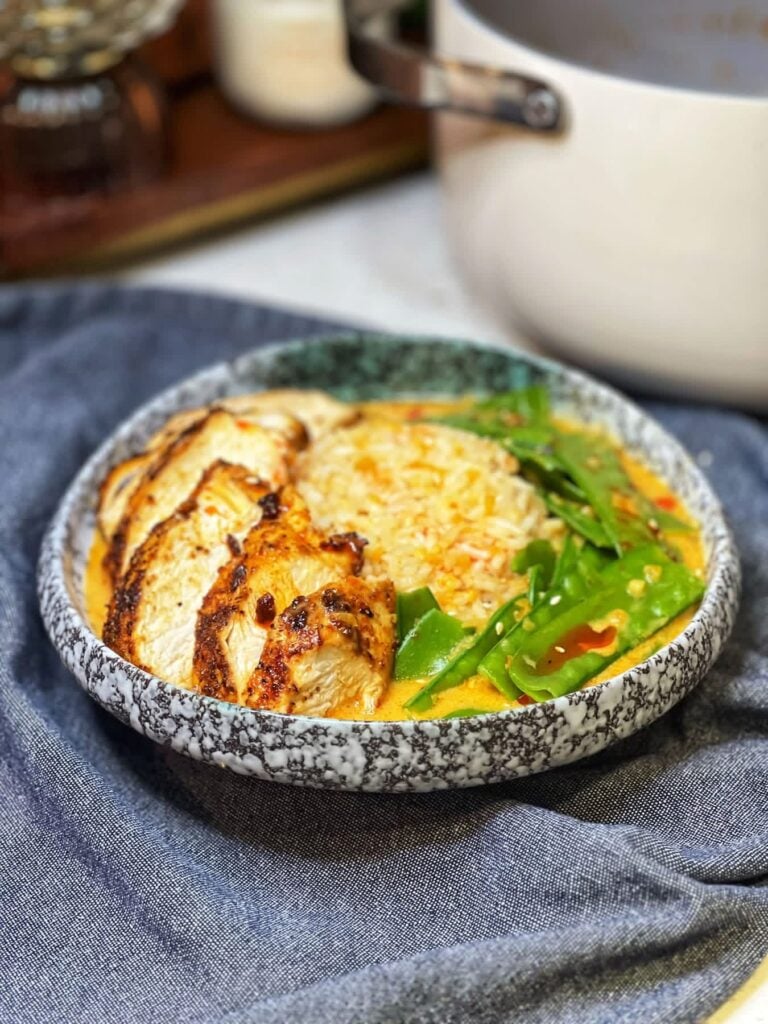 A curry chicken rice bowl. Steamed rice is in a bowl with snow peas, chicken and a creamy broth.